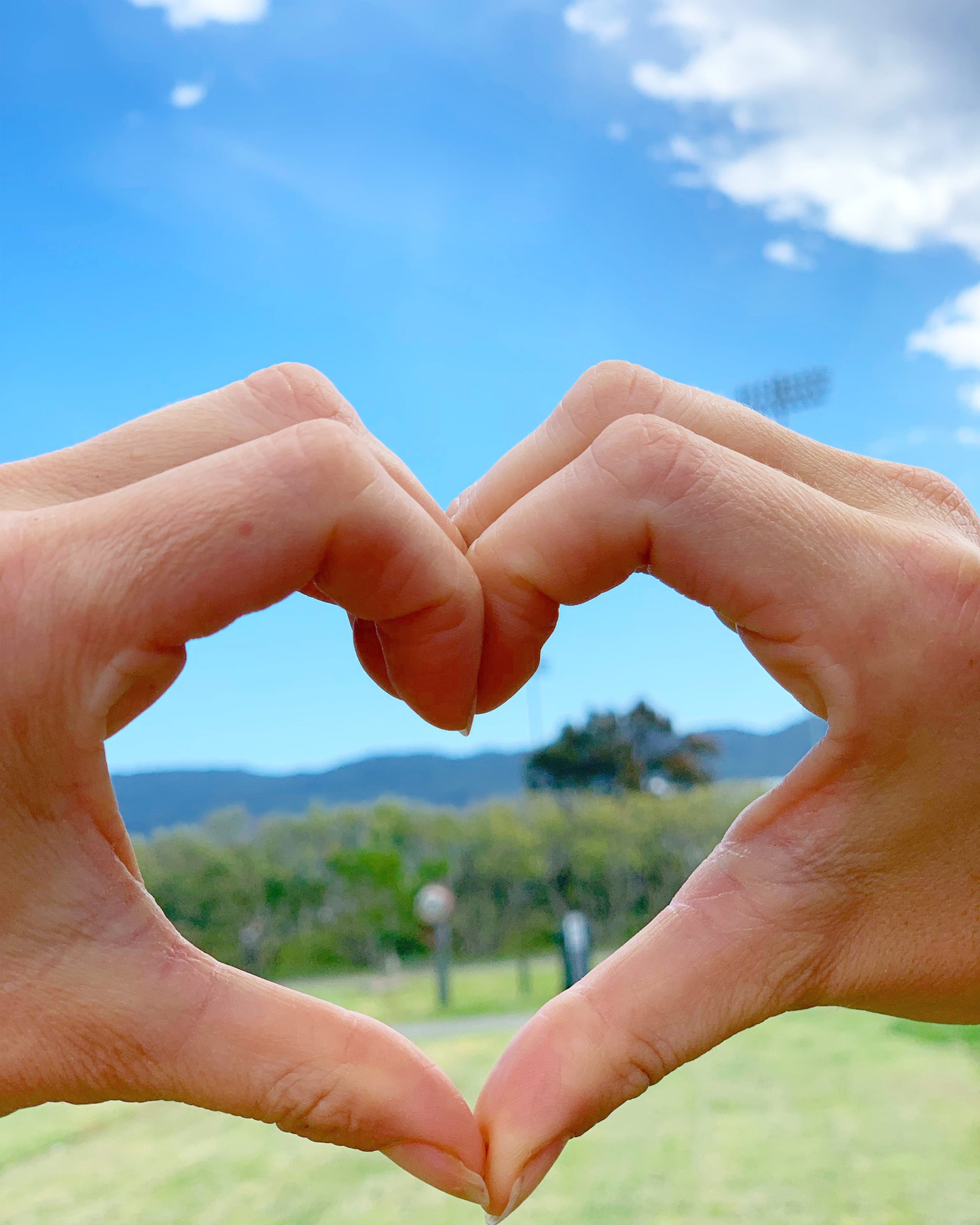 Hands making a love heart shape in front of a mountain