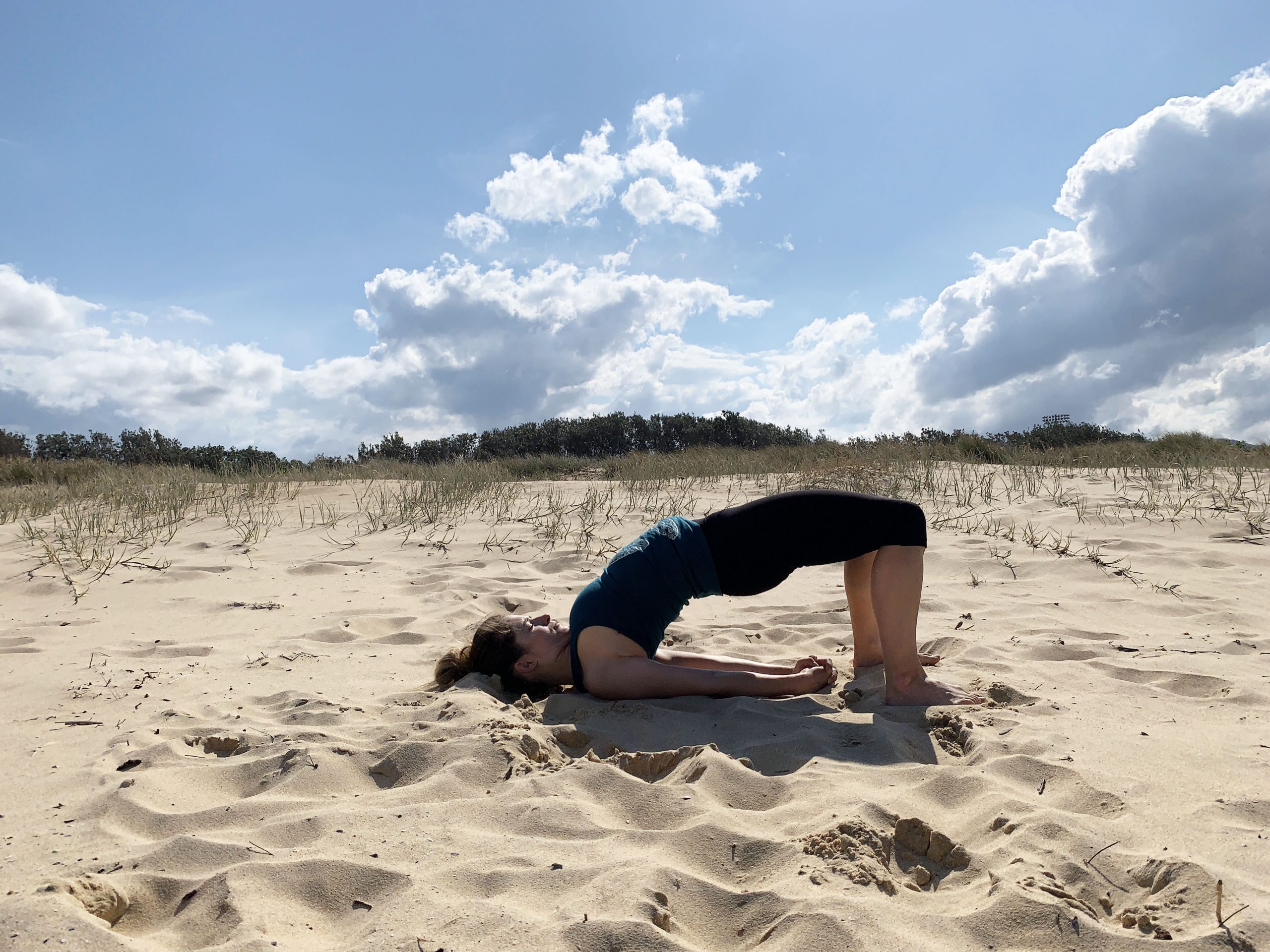 Woman doing Bridge Yoga Pose at the beach