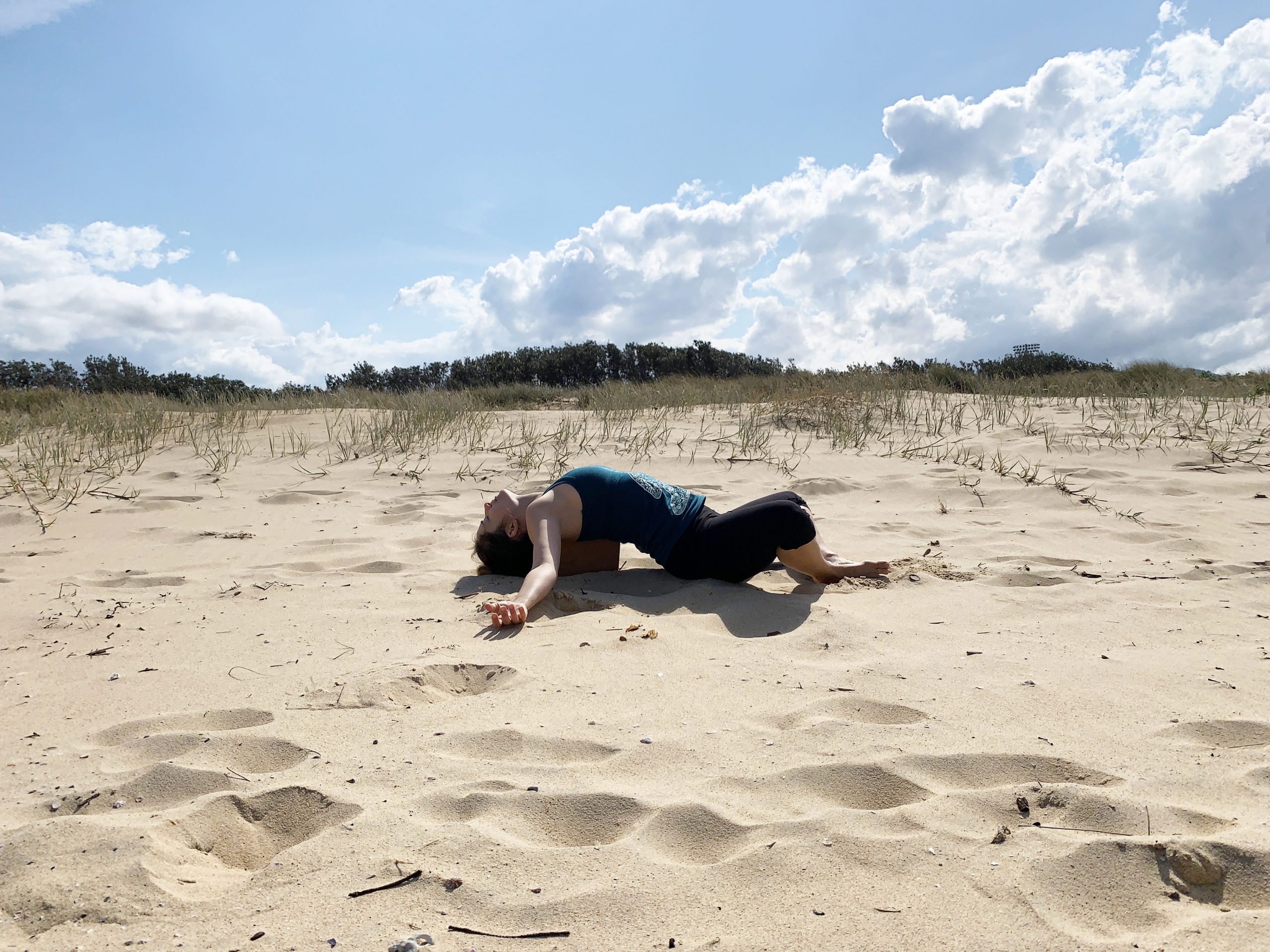 woman doing a heart opening yoga pose at the beach